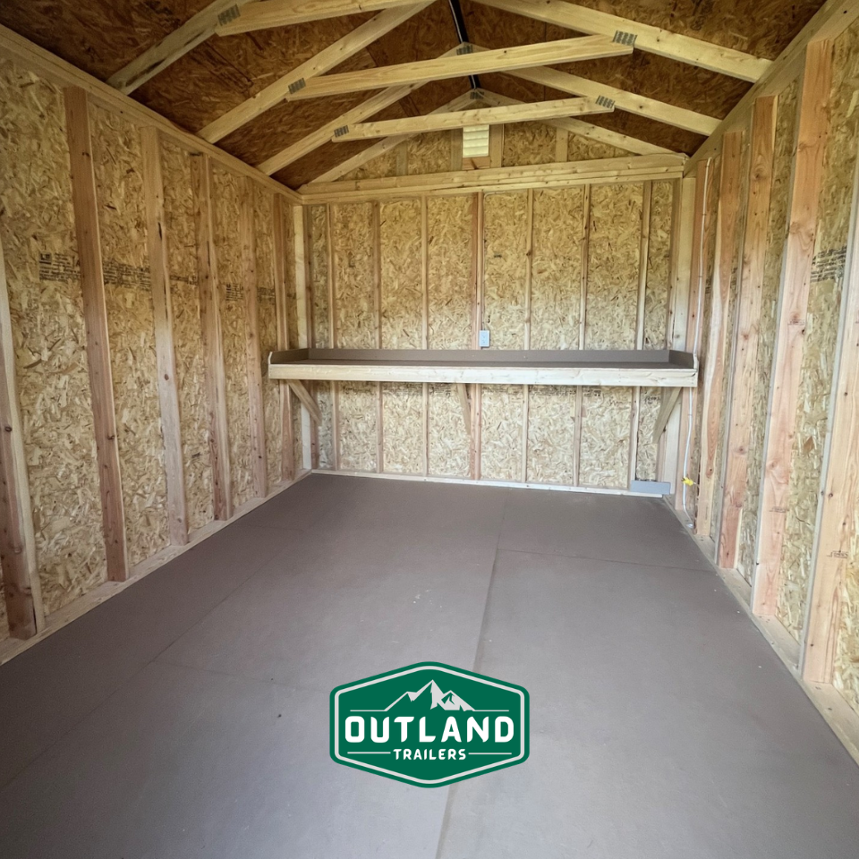 Outland Trailers 10x12 utility shed with gray metal roof and wooden walls, shown from an angle with a double door entrance.