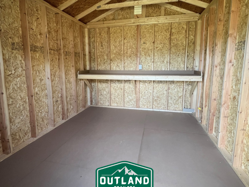 Outland Trailers 10x12 utility shed with gray metal roof and wooden walls, shown from an angle with a double door entrance.