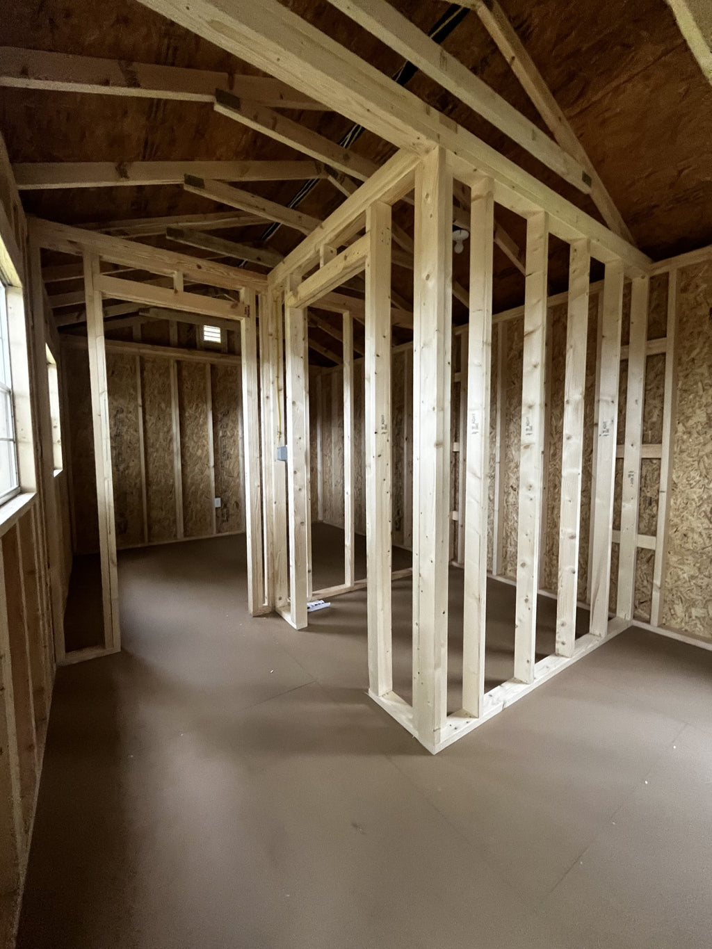 Outland Trailers 12x36 tiny home shell with wooden exterior and large front window, ready for customization and interior finishing.