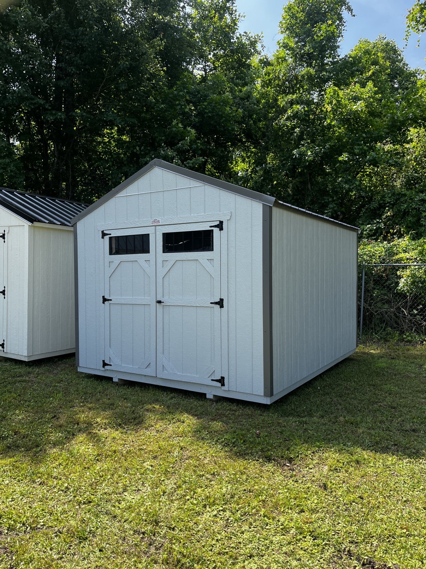 Outland Trailers 10x12 utility shed with metal walls and door, outdoor storage solution for gardening tools and equipment.