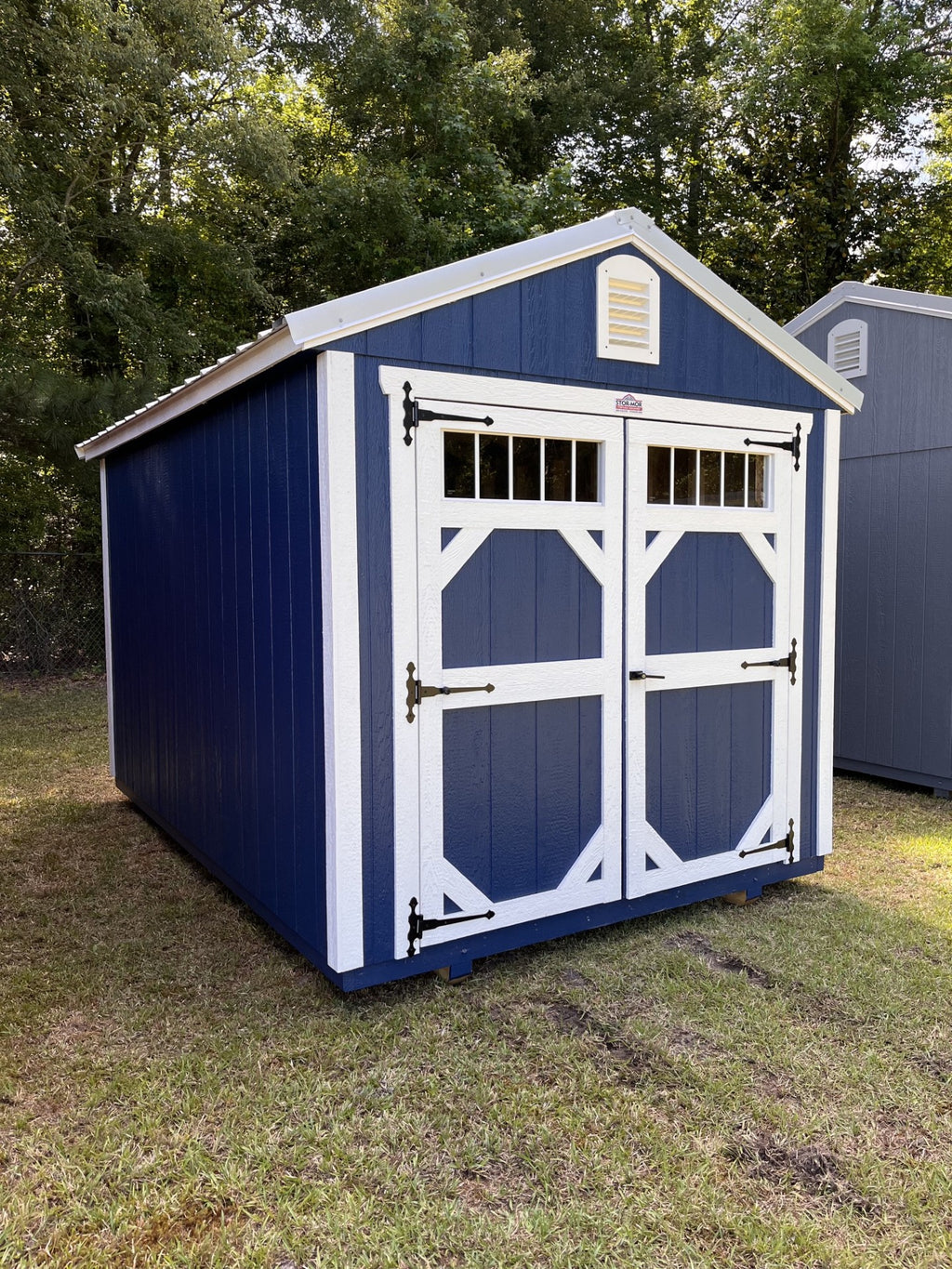Outland Trailers 8x12 garden shed with wood-paneled exterior and metal roof, set on a grassy lawn.