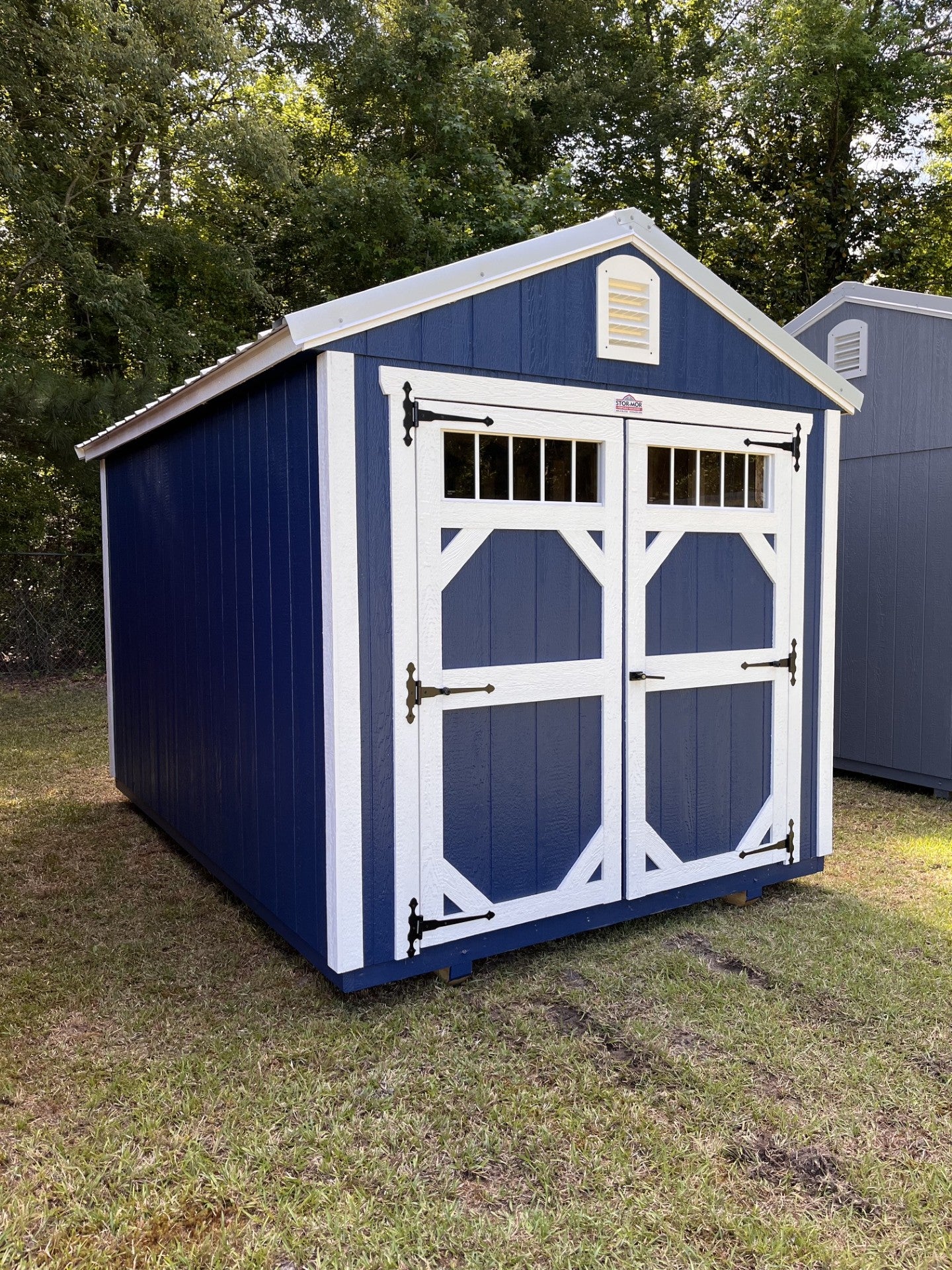 Outland Trailers 8x12 garden shed with wood-paneled exterior and metal roof, set on a grassy lawn.
