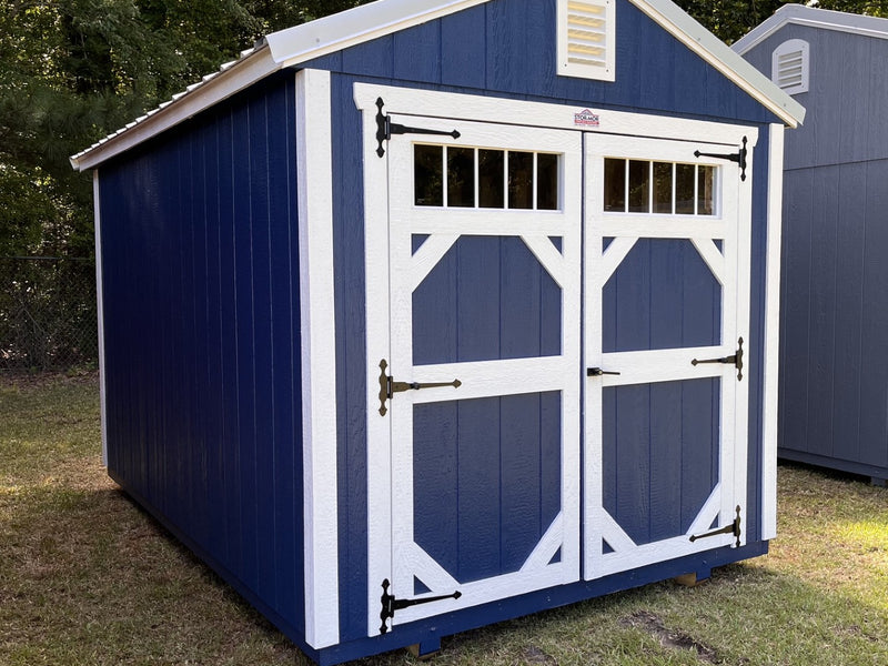 Outland Trailers 8x12 garden shed with wood-paneled exterior and metal roof, set on a grassy lawn.