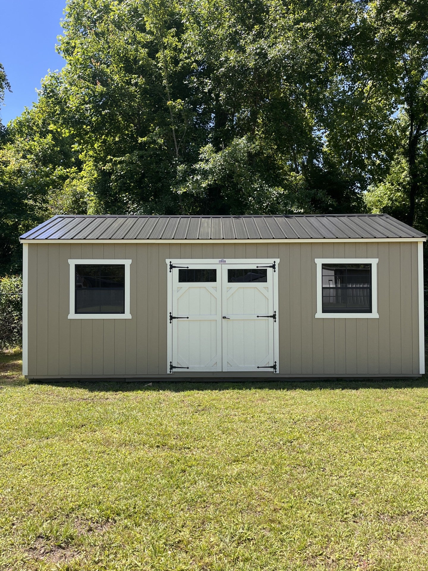 Outland Trailers 12x24 side utility shed with metal walls and door, set on a gravel surface in a rural outdoor setting.