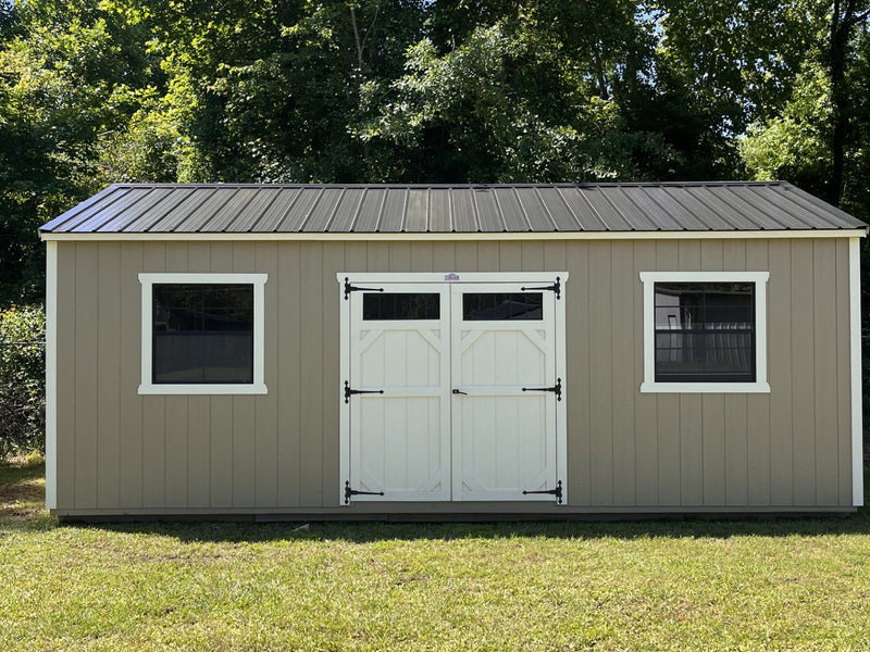 Outland Trailers 12x24 side utility shed with metal walls and door, set on a gravel surface in a rural outdoor setting.