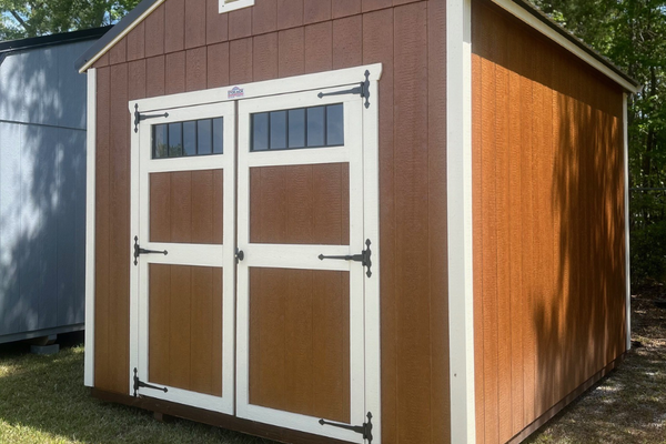 Outland Trailers 10x12 utility shed with wooden door and metal roof, ideal for storage and outdoor use.