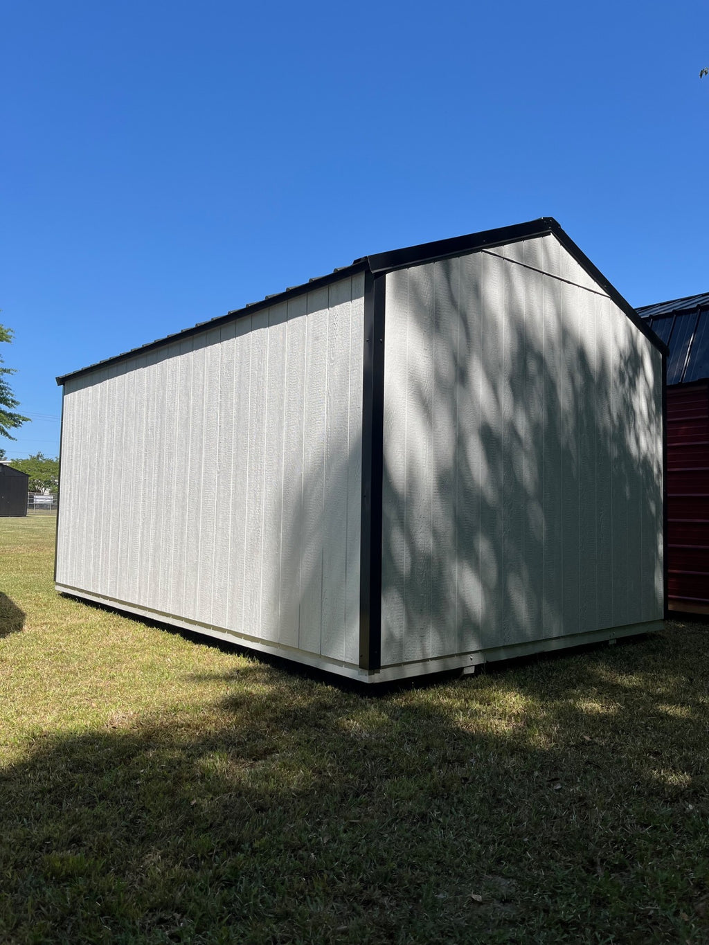 Outland Trailers 10x16 Tru-Valu Utility Shed with metal roof and double doors, placed on a grassy outdoor area.